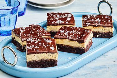 Buckeye Brownies with sea salt garnish, cut into pieces on a blue dish, with blue cups and small white plates 