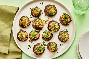 Platter of stuffed mushrooms garnished with parsley on a green surface. Serving plates, a green napkin and a green glass of sparkling water 