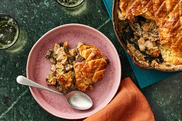 Serving of Mushroom Pot Pie on a muted pink plate,with full pot pie in a skillet on the side. 2 glasses of sparkling water, and a rust colored napkin