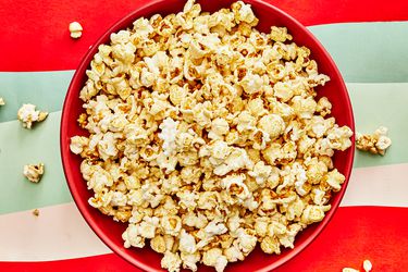 Red bowl full of Kettle corn on a red and green striped surface 