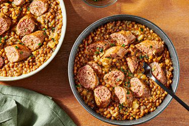 2 bowls of pressure cooked lentils and sausage on a wooden tabletop, with a soft turquoise napkin, and small bowl of parsley for garnish to the sides. 