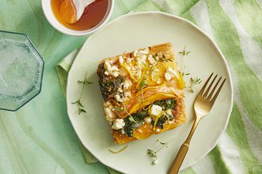 slice of savory crinkle pie on a plate with green textiles, a sparkling water, and a small bowl of honey on the side 