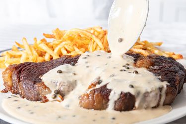 Steak and french fries with Green Peppercorn sauce being poured on top 