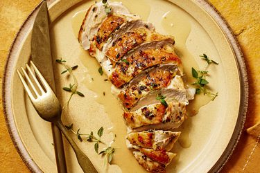 Sliced chicken breast with sauce on it and fresh thyme, on a yellow plate, yellow napkin, and yellow textile