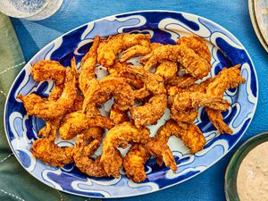 Southern Fried Shrimp on a blue printed plate, with dip, and sparkling water, and a blue textile. 