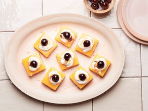 Amaretto Lemon Bars on a warm blush colored plate and tile surface. smaller serving plates and a small bowl of cherries to the side