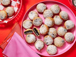 pink platter of fried oreos, two with bite taken out and middle showing. Red background and red basket of oreos on the side, and pink and red napkins. 