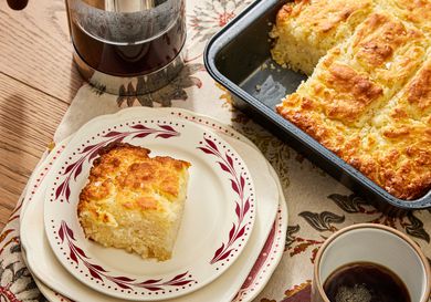 Butter swim biscuit tray, with one piece on a stack of white and red plates, on a cozy tablecloth, with a french press and a cup of coffee