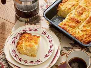 Butter swim biscuit tray, with one piece on a stack of white and red plates, on a cozy tablecloth, with a french press and a cup of coffee