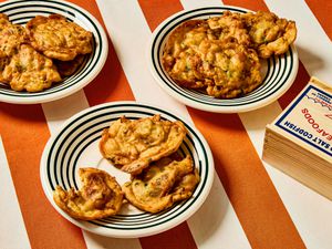 3 plates of bacalaitos and a wooden box of cod fish on red and white striped tablecloth 