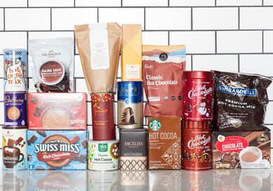 group of different hot chocolate packages stacked together on white surface with white tile background