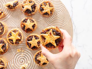 Decorative platter of baked minced pies, with hand holding one pie close up 