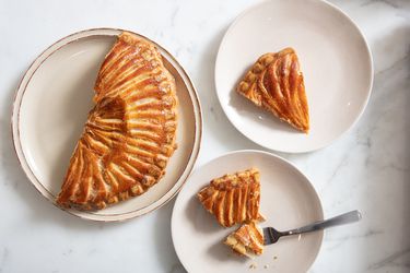 2 plates of Galette des Roi, one with a fork full of cake. A third plate with the remaining galette on it 