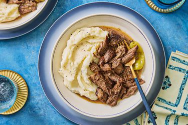 Mississippi Roast with mashed potatoes on blue plates and blue surface, Napkins and cups are blue and gold decor