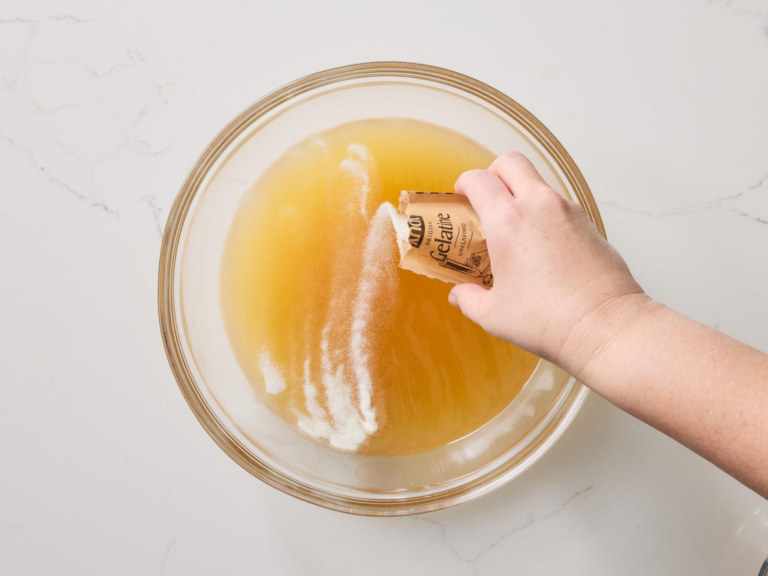 Adding a packet of gelatin to broth mixture 