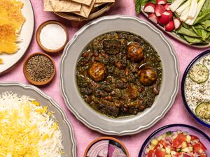 Overhead of Khoresh E Ghormeh Sabzi surrounded with rice, dips, and vegetables 