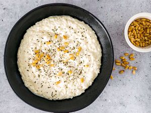 Labaniyeh bil Ruz in a black bowl with toasted pine nuts