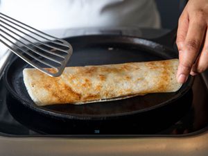 Rolling a cooked dosa on a cast iron griddle