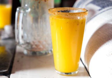 A rimmed pint glass of bright-orange pulque.