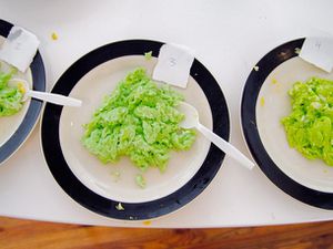 Three side-by-side plates of scrambled eggs that have been dyed with green food coloring. The eggs are part of a taste and quality test.