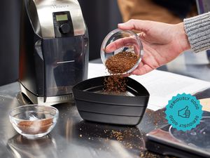 A hand pouring coffee grounds into a sifter. A coffee grinder is beside the sifter.