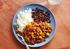 A blue ceramic plate with picadillo, white rice, and black beans.