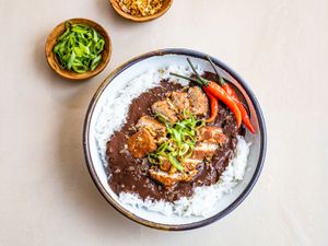 Dinuguan served over bowl of rice, garnished with chiles and sliced scallions