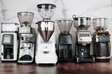 Six espresso grinders lined up against a marble backdrop