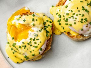 Two foolproof Eggs Benedict on a ceramic plate. The yolk is broken on the left Benedict, showing that the eggs has been properly poached.