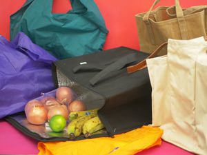 Numerous reusable grocery bags, with onions, a lime, and bananas spilling out of one.