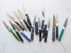 Numerous paring knives on a marble kitchen countertop.