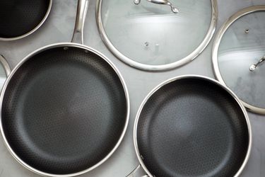 three hexclad skillets in different sizes with lids on a gray surface