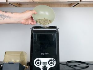 green coffee beans being loaded into the top of an air coffee roaster