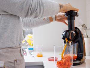 a person using a slow juicer to juice carrots