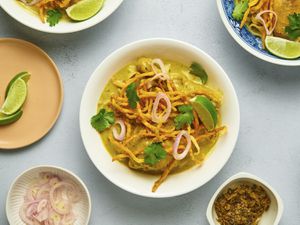 Khao soi gai in a white ceramic bowl, with additional small bowls containing condiments on the periphery.