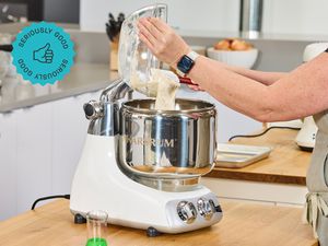 A person adding dough to an Ankarsrum stand mixer.