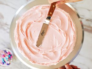 A person using an offset spatula to frost a cake on a cake stand