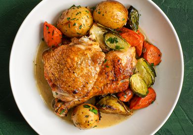 A white ceramic dish holding pan-roasted chicken and vegetables in jus.