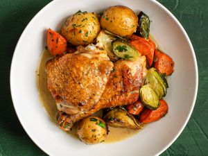 A white ceramic dish holding pan-roasted chicken and vegetables in jus.