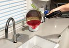 A person using a clip-on strainer to water from pasta noodles into a sink.