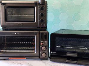 three countertop smart ovens on a marble surface with a teal green tile background