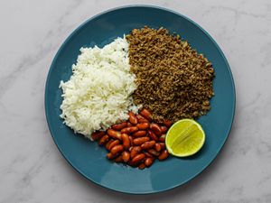 SalpicÃ³n, white rice, red kidney beans, and a slice of lime on a blue plate on a marble counter.