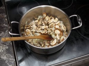 a rondeau on a stove with mushrooms and onions and a wooden spoon