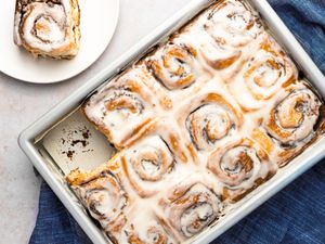 Cinnamon rolls in pan with a roll served on a plate peeking into frame