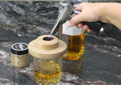 a person using a butane torch to light wood chips in a wooden drink topper