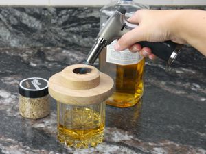 a person using a butane torch to light wood chips in a wooden drink topper