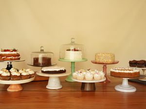 Nine cake stands holding cakes and cupcakes sit on a wooden surface