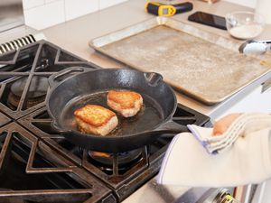 A person searing meat in a cast iron skillet on the stovetop