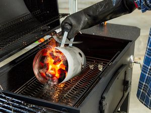 A person adding charcoal to a charcoal grill