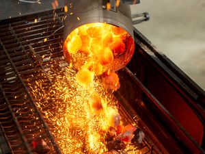 Charcoal being poured into a charcoal grill from a chimney starter.